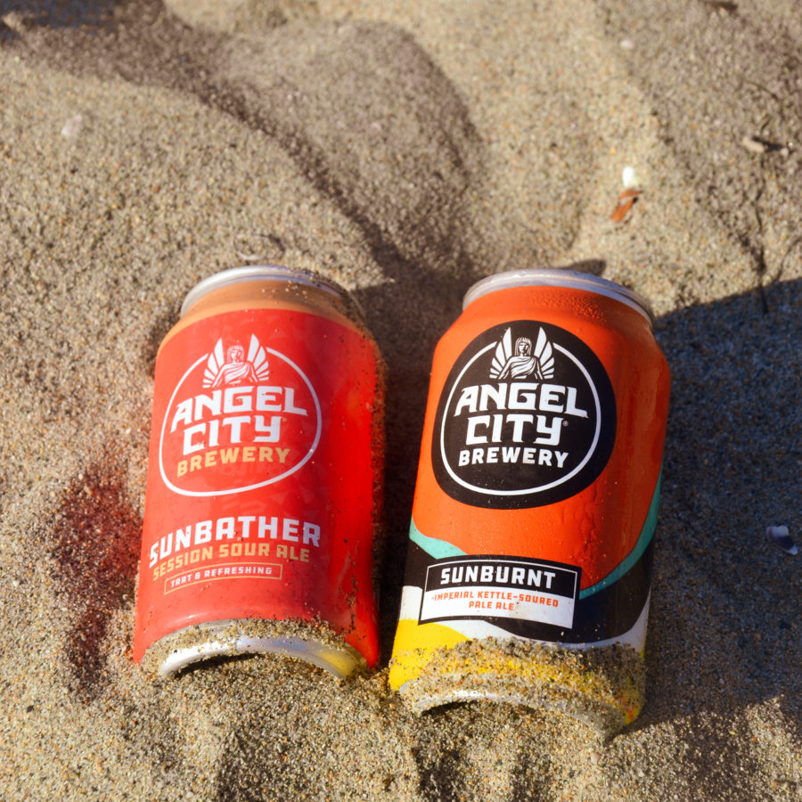12oz can of Sunbather Session Sour Ale next to a 12oz. can of Sunburnt Imperial Sour Ale in the sand