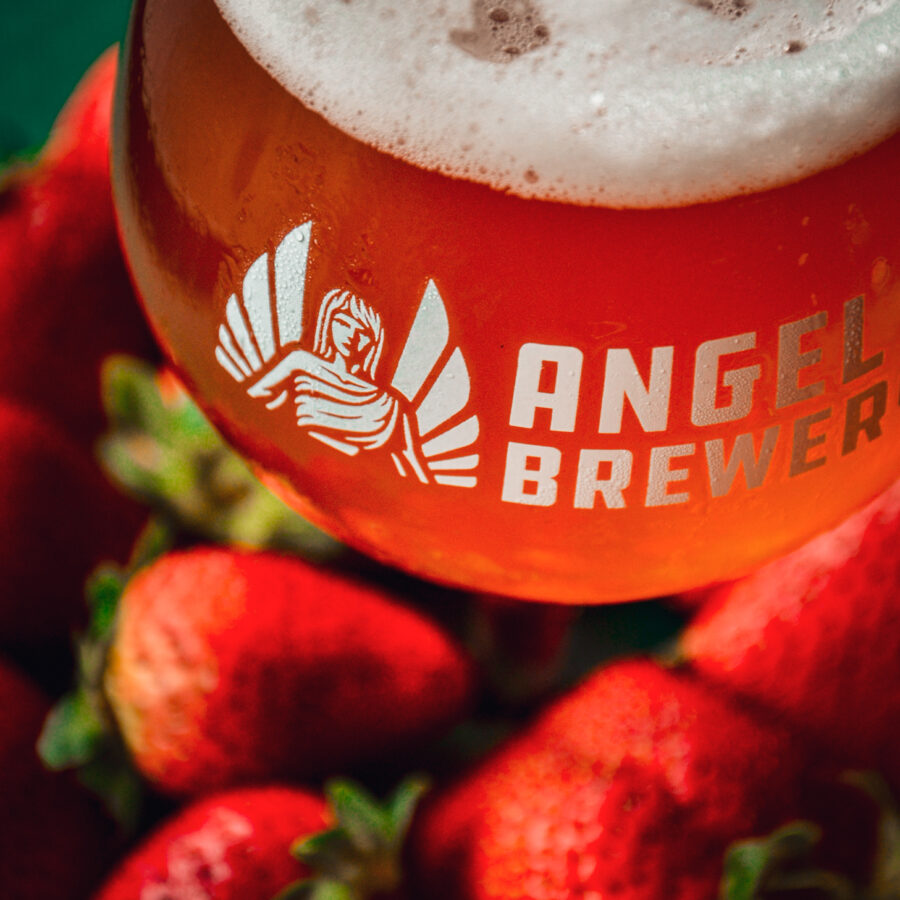 A close-up shot of a pint of Angel City Brewery's Strawberry Gose, next to a bed of ripe strawberries