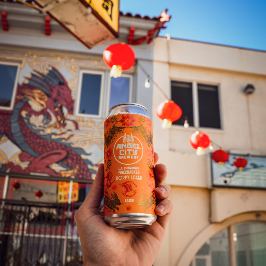 Hand hoisting 1 16oz can of Angel City brewery x Firecracker 10k's collab beer "Hoppy Lager" in LA's Chinatown District